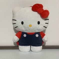 a hello kitty stuffed animal with a red bow on its head and blue overalls