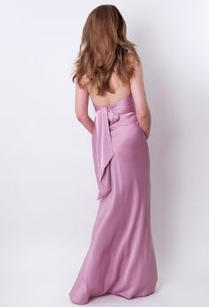 the back of a woman in a long purple dress with a bow on her shoulder