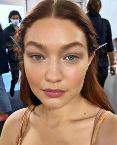 a woman with brown hair and blue eyes is looking at the camera while she has scissors in her ear