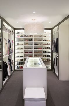 a walk in closet filled with lots of shoes and clothing on shelves next to a white bench