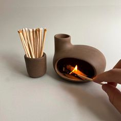 a person holding a match stick in front of a small clay pot with matches sticking out of it