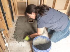 a woman is pouring cement into a bucket on the floor in front of a door