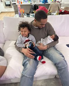 a man sitting on top of a white couch next to a little boy holding a baby