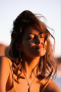 a woman with her eyes closed wearing a necklace and earring, looking off into the distance