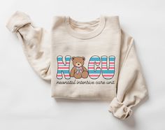 a white shirt with a brown teddy bear on it's chest and the words now written in red, white, and blue