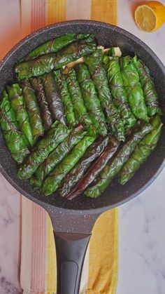 a pan filled with cooked green vegetables on top of a table next to an orange slice