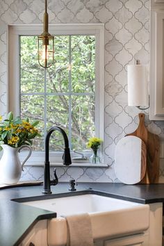 a kitchen sink under a window next to a wooden cutting board and vase with flowers