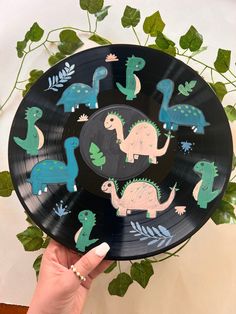 a person holding up a black plate with dinosaurs painted on it and leaves around the edges