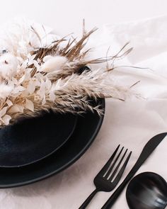 a black plate topped with white flowers next to two forks and spoons on top of a table