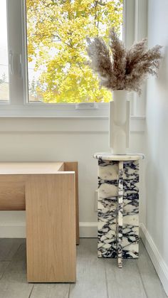 a white vase with dried plants in it next to a table and window sill