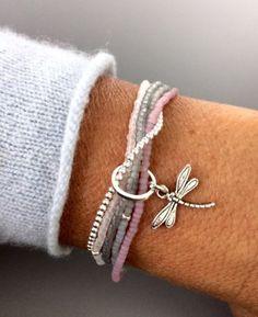 a woman's arm with three bracelets and a dragonfly charm on it