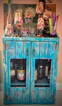 a blue cabinet with many bottles and glasses on top of it in front of a wall