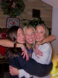 three women hugging each other in front of a fireplace