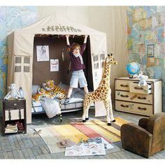 a young boy standing on top of a bed next to a giraffe