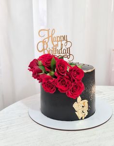 a black and gold birthday cake with red roses on the top is sitting on a white table