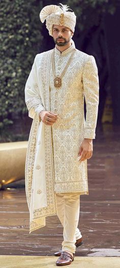 a man in a white outfit standing on a wooden floor with his hands in his pockets