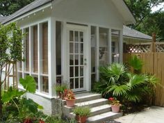 a small white house surrounded by plants and trees