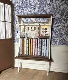 a wooden shelf filled with lots of different colored fabrics next to a wallpapered room