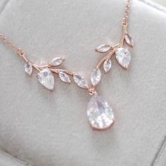 a rose gold necklace with white stones and leaves hanging from it's center piece