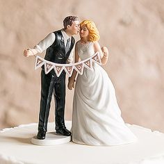 a bride and groom figurine on top of a wedding cake with bunting