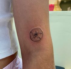 a small sand dollar tattoo on the arm