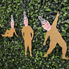 three people wearing party hats hanging on a string with green bushes in the back ground