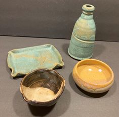 three ceramic bowls and two vases sitting on a gray surface next to each other