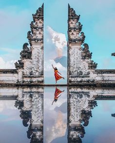 a woman in a red dress is standing at the entrance to an ancient building with its reflection