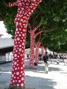 red and white polka dots are on the trees in front of people walking down the street