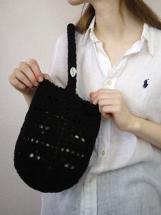 a woman is holding a black crocheted handbag in her right hand and wearing a white shirt