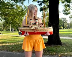 a woman in yellow shorts holding a model boat