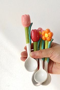 a hand holding three spoons with flowers on them and candy canes sticking out of them