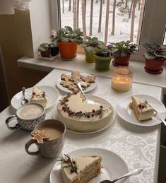 a table topped with cakes and desserts next to a window filled with potted plants