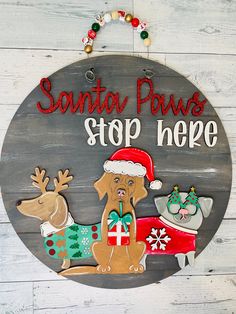 a wooden sign that says santa paws stop here with two dogs and presents on it