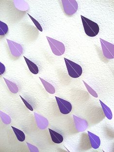 purple and white paper raindrops are hanging from the ceiling in front of a wall