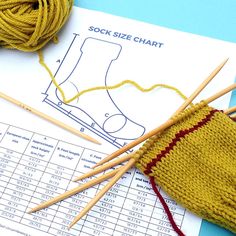 a pair of knitting needles next to a sock size chart with yarn on the table