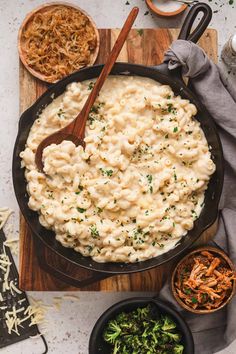 a skillet filled with macaroni and cheese on top of a wooden cutting board