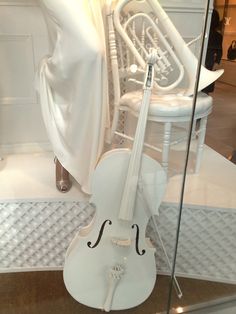 a white violin sitting on top of a glass case next to a chair and table