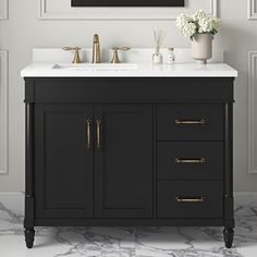 a bathroom vanity with marble counter top and gold faucet, framed art above it