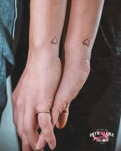 two people holding hands with small tattoos on their wrists and fingers, both wearing matching rings