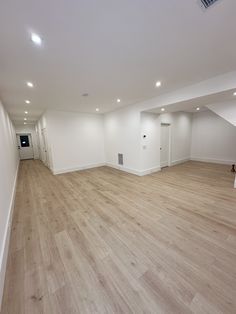 an empty room with hard wood flooring and white walls in the center is lit by recessed lighting