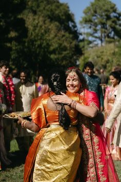 two women hugging each other in front of a group of people on the grass and trees