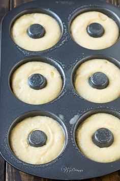 a muffin tin filled with yellow batter and black plastic knobs, on top of a wooden table