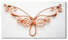 a copper wire butterfly brooch sitting on top of a white surface with an intricate design