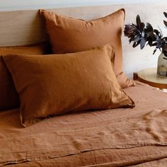 a bed with brown linens and pillows on it next to a vase filled with flowers