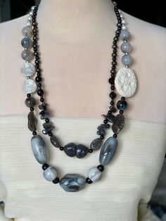 Elegant harmony of grades of black/ grays  and white in a natural look stones, mixture of sizes of beads , pearls and stones that creates a contrast of a beautiful streamlined necklace in tow rows, adorned with huge white natural stone, finished with an adjustable silver color chain. Adjustable Gray Gemstone Beaded Necklace, Elegant Gray Gemstone Beads Necklace, Elegant Gray Faceted Beads Necklace, Silver Multi-strand Gemstone Beads, Black Multi-strand Necklace With Faceted Beads, Marble Colors, Grey Stone, Stone Necklace, Stone Color