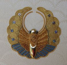 a gold and blue beaded necklace with an egyptian bird on it's back