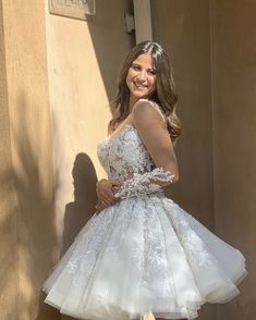 a woman standing in front of a wall wearing a white dress