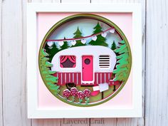 a paper cut out of a camper with trees and flowers on the front, in a white frame