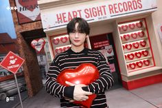 a person holding a heart shaped object in front of a store with red and white signs